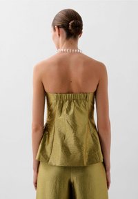 Stropfri peplum top i metallisk guldstof, der har en tekstureret overflade og en sammenslynget ryg, parret med matchende vide bukser.