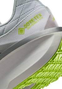 Gros plan sur le talon d'une basket grise et blanche avec le logo vert Gore-Tex Invisible Fit et la semelle extérieure texturée vert vif.