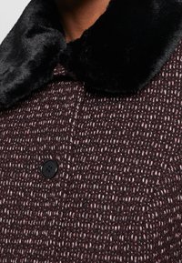 Cappotto in misto lana di un intenso bordeaux scuro con una finitura testurizzata, dotato di un colletto in pelliccia ecologica nera e di un bottone nero.