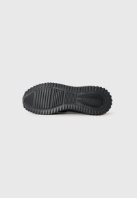 Zwarte rubberen sneakerzool met horizontale en verticale groeven, gekenmerkt door een verhoogde rand. Geribbelde grippatroon over het gehele oppervlak.