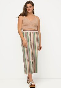 Béžový pletený crop top s výstřihem do V a vzorované nohavice s širokými nohavicemi, které mají vertikální vícebarevné pruhy. Boty jsou světlé s přezkou.