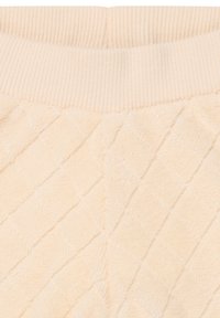 Loungewear w kolorze kremowym z pionowym ściągaczem w pasie. Materiał charakteryzuje się miękką, puszystą teksturą oraz diamentowym wzorem pikowania.