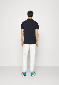 Mörkblå pikétröja med korta ärmar, i kombination med vita byxor och flerfärgade sneakers, som visar en avslappnad outfit från baksidan.