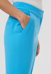Heldere blauwe broek gemaakt van een gladde stof, met een brede tailleband, schuine zijzakken en nette stiksels.