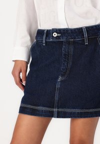 Mørk denimskjørt med høy midje, frontknappåpning og hvite sømdetaljer, med rett snitt og uten mønstre.