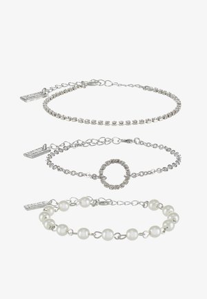 Trois bracelets en argent : un avec des pierres précieuses transparentes, un avec un accent circulaire, et un avec des perles blanches, ornés de maillons de chaîne délicats.