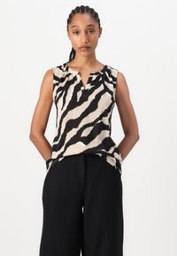 Ermeløs topp i beige med svarte og hvite zebra-striper. Har en avrundet halslinje og en subtil spalte foran. Myk stoffkvalitet.