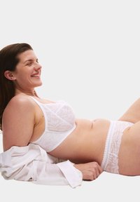 Bralette bianco in pizzo e mutandine abbinate con motivi floreali, texture trasparente e delicato bordo in pizzo, abbinati a una camicia bianca sbottonata.