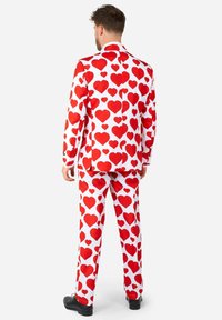 Červený a biely oblek s veľkými červenými srdcami na saku aj nohaviciach, strih na mieru, s čiernymi topánkami.
