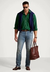 Grønn skjorte med knapper, marineblå vest, lyseblå jeans, brune skinnsko og en brun skinnveske. Tilbehør inkluderer solbriller og klokke.