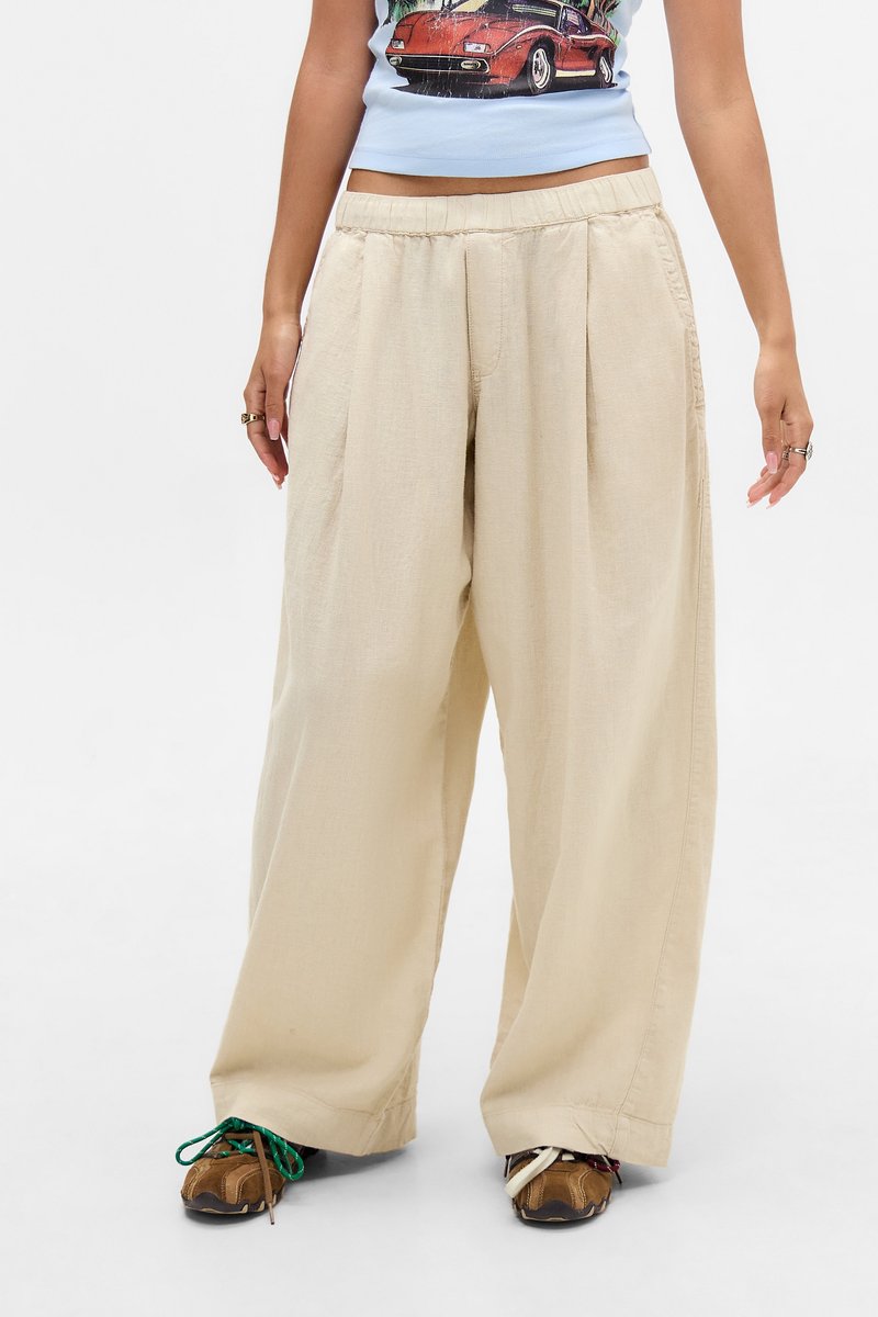 Persona con pantalones anchos beige, zapatillas marrones con cordones desiguales y un crop top azul con un gráfico de coche rojo.