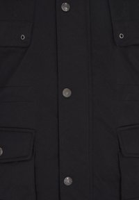 Zwarte jas aan de voorkant met twee klepzakken, metalen drukknopen met gravure, en gestikte naden.