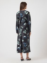Kvinna klädd i en lång svart klänning med blå och vita abstrakta blommönster, står med ryggen vänd mot kameran.