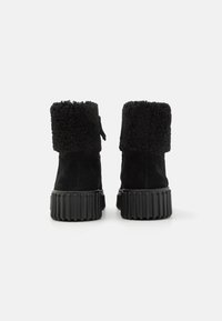 Botas de tobillo de ante negro con un suave collar de piel de lana negra, que cuentan con una suela de goma estriada y una lengüeta para ponerlas fácilmente.