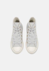 Zapatillas altas de lona gris claro con punteras de goma blanca. Presenta ojales dorados y cordones planos. Textura suave en toda la superficie.