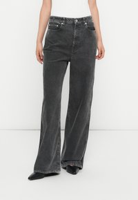 Jean en denim noir taille haute avec jambes larges, dot�és d'une fermeture à bouton et à zip, de cinq poches et d'une texture légèrement déchirée.