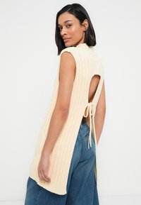 Haut sans manches en maille côtelée de couleur pêche douce, avec dos ouvert et liens, accompagné d'un pantalon en denim bleu ample.