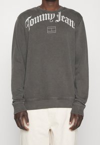 Šedá mikina vyrobená z bavlněné směsi, s bílým logem a emblémem "Tommy Jeans" na hrudi, s žebrovanými manžetami a spodním lemem.