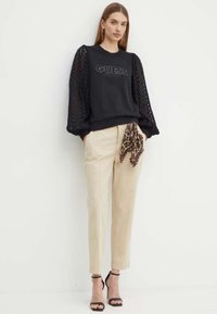 Felpa nera con maniche texture e gonfiate. Pantaloni beige con una sciarpa a stampa leopardata annodata. Sandali neri con tacco alto.