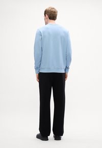 Ανοιχτό μπλε φούτερ με στρογγυλή λαιμόκοψη και μακριά μανίκια, συνδυασμένο με μαύρα παντελόνια σε φαρδιά γραμμή και μαύρα αθλητικά παπούτσια. Απλός σχεδιασμός, χωρίς ορατά λογότυπα.