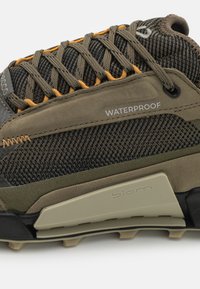 Wasserdichter Wanderschuh mit einem strukturierten oberen aus olivgrünem und schwarzem Stoff, verstärktem Absatz und orangefarbenen Schnürsenkeln. Verfügt über eine Gummilaufsohle für Rutschfestigkeit.