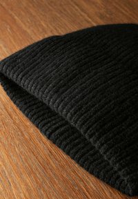 Zwarte gebreide beanie muts met een ribbelstructuur, gemaakt van zacht materiaal, weergegeven op een houten oppervlak.