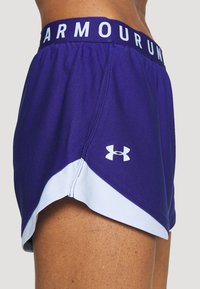 Fialové sportovní šortky se světle modrým lemem, elastickým pasem s bílým nápisem "ARMOUR" a bílým logem Under Armour na boku.