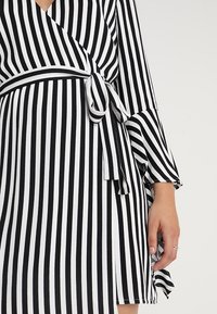 Schwarz-weißer gestreifter Wickelkleid mit gebundenem Taillenbereich, ausgestellten Ärmeln und V-Ausschnitt, aus weichem Stoff mit fließendem Design.