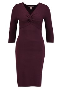 Robe en tricot d'un profond bordeaux avec des manches trois-quarts, dotée d'un détail en nœud torsadé à la taille et d'une silhouette ajustée.