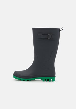 Botte de pluie noire mi-mollet avec semelle crantée verte, bride réglable avec boucle sur la tige, et languette d'extraction en haut à l'arrière.
