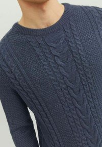 Mørkeblå strikket sweater med teksturerede mønstre, der har et flettet strikkedesign langs fronten og ribbet rund halsudskæring.