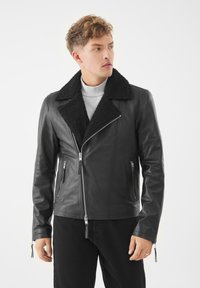 Černá kožená bunda s ovčí vlnou na límci, zapín�ání na zip a kapsy, s elegantním designem a texturovanými detaily.