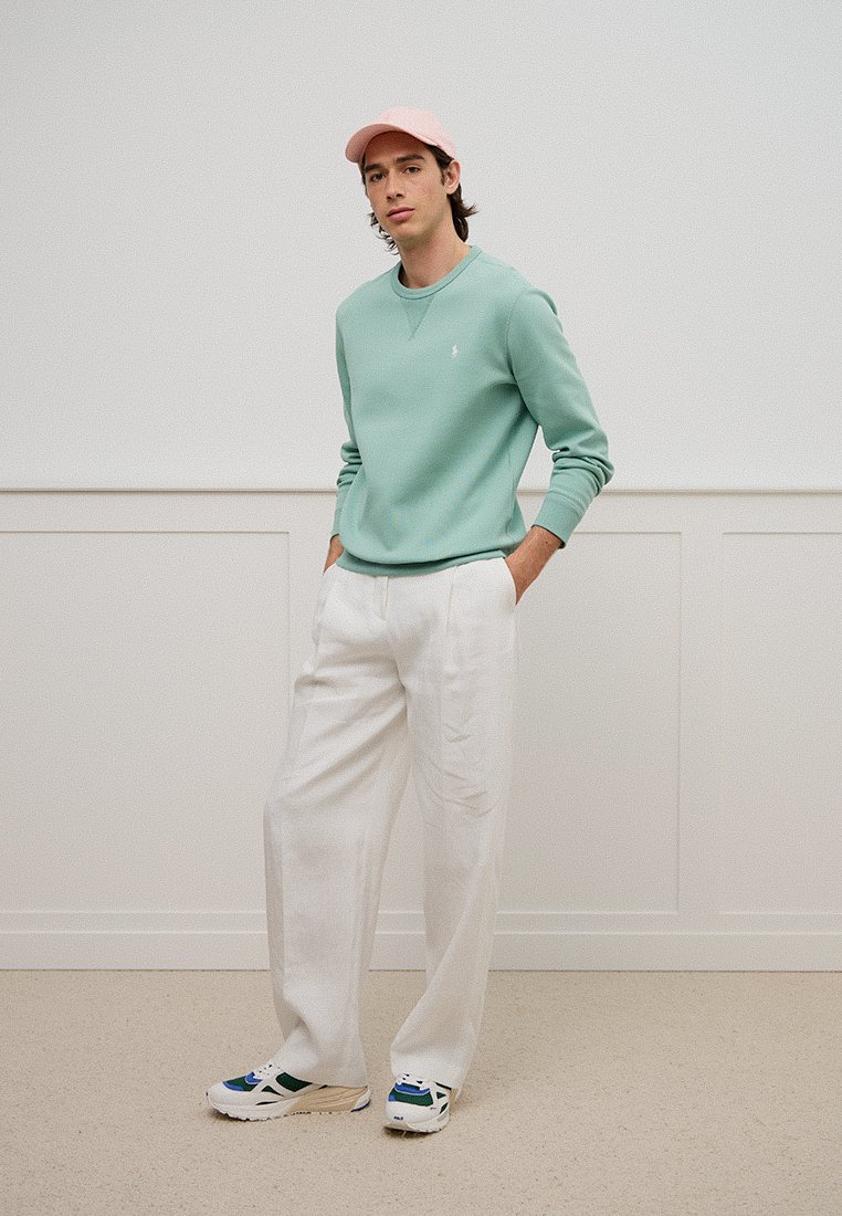 Mintgrüner Pullover, weiße weit geschnittene Hosen und mehrfarbige Turnschuhe. Verfügt über eine rosa Mütze und ein kleines Logo auf dem Pullover.