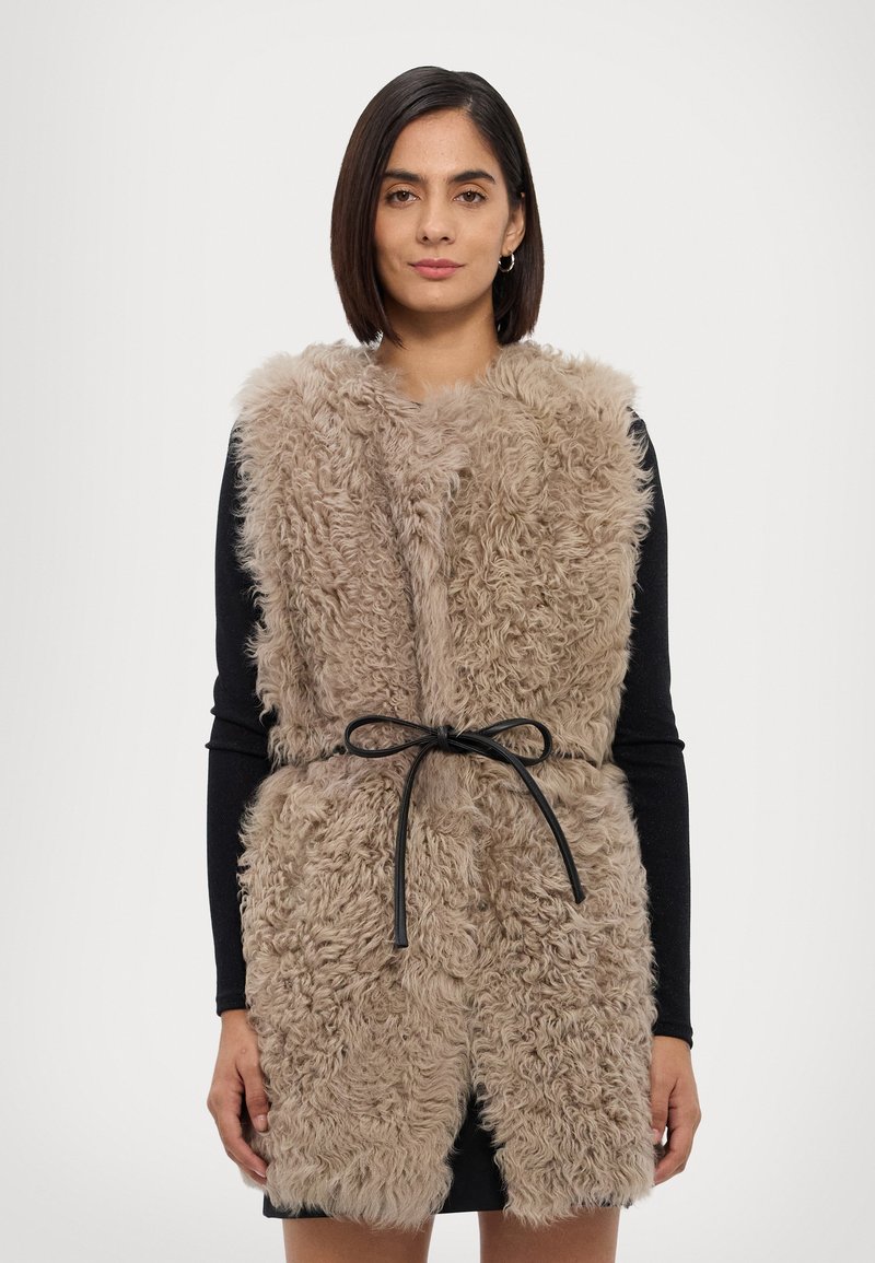 Nep-bont gilet in beige met een gestructureerde, harige uitstraling. Heeft een zwarte riem in de taille en een mouwloos ontwerp.