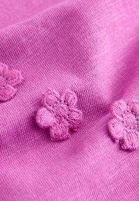 Világos rózsaszín szövet, puha tapintású, három sötétebb rózsaszín hímzett virággal díszítve. A mintán homogén, sima kötésminta látható.