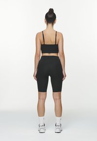 Zwarte sportbh met dunne bandjes, gecombineerd met zwarte fietsshorts met hoge taille tot de knieën. Witte sportsokken en schoenen maken de outfit compleet.