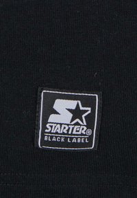 Juoda medžiaga su tekstūriniu paviršiumi turi kvadratinį logotipo pleistrą. Pleistras yra baltas ir pilkas, jame užrašyta "STARTER" ir pavaizduota žvaigždutė.