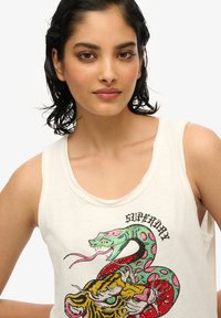 Biała koszulka bez rękawów z żywym, wyszywanym wzorem węża i tygrysa, z wielokolorowymi akcentami i o zaokrąglonym dekolcie.