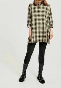 Grøn og beige plaid tunika med en knapkrave og trekvartærmer, parret med sorte leggings og sort knæhøje støvler.