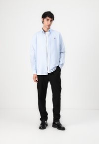 Light blue button-up shirt, long sleeves, white inner shirt visible underneath, paired with black trousers and black shoes.