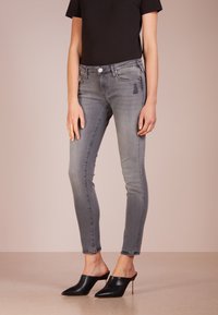 Jeans skinny grises con una textura desgastada, cinco bolsillos y sutiles detalles deshilachados, combinados con mules de tacón negro y punta afilada.