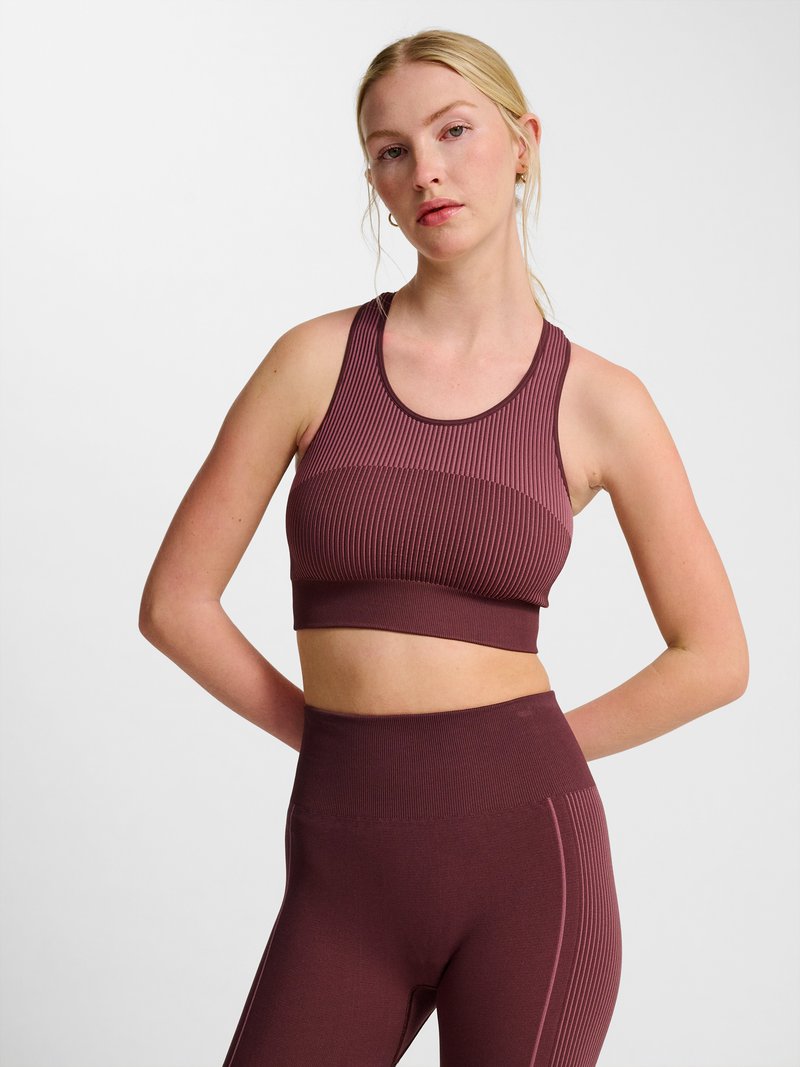Ung kvinde med blondt hår bundet tilbage iført en ribbet ærmeløs croptop og højtaljede legging i mørk mauve.