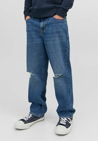 Ljusa denimjeans med lös passform, slitna knädetaljer och en lätt blekning, kombinerade med marinblå sneakers med vita gummiklädda sulor.