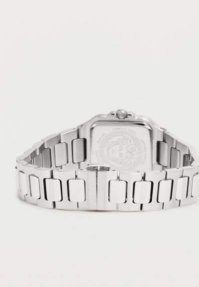 Montre bracelet en métal argenté avec cadran carré et logo gravé sur la boucle et la plaque arrière, présentée sur fond blanc.