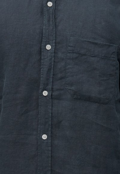 Σκούρο γκρι πουκάμισο με κουμπιά, λευκά κουμπιά, αριστερή τσέπη στο στήθος και διακριτικό κεντημένο λογότυπο κοντά στο κάτω δεξί μέρος.