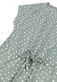 Groene jurk met witte stippen, gemaakt van zachte stof. Heeft korte mouwen en een koord taille voor een verstelbare pasvorm.