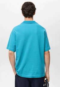 Turkizna polo majica s kratkimi rokavi in ribastim ovratnikom. Mehka tekstura, sproščen kroj in enostaven dizajn brez vidnih vzorcev ali logotipov.