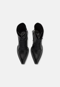 Bottes noires en cuir à hauteur de cheville avec un bout pointu, un laçage à l'avant et une fermeture éclair sur le côté ; tige texturée et finition lisse et brillante.
