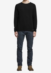 Svart långärmad skjorta i kombination med mörkblå jeans. Skjortan har en rund halsringning och är gjord av ett mjukt material. Bruna ankelstövlar fulländar looken.