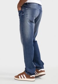 Τζιν παντελόνι σε μέτριο πλύσιμο με χαλαρή εφαρμογή, ελαφριά ξεθώριασμα και πέντε τσέπες. Συνδυάζεται με καφέ σουέντ αθλητικά παπούτσια με λευκές ρίγες.